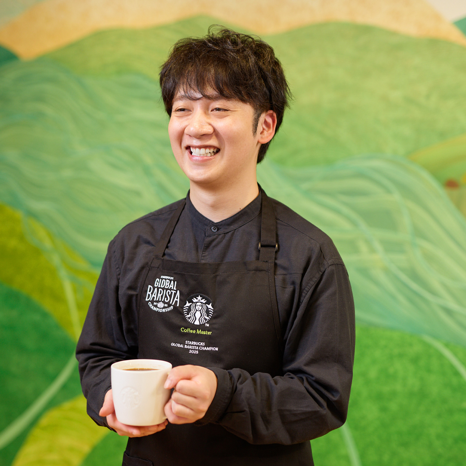 コーヒーアンバサダーの下出さんが、抽出したコーヒーを片手にインタビューを受けている様子