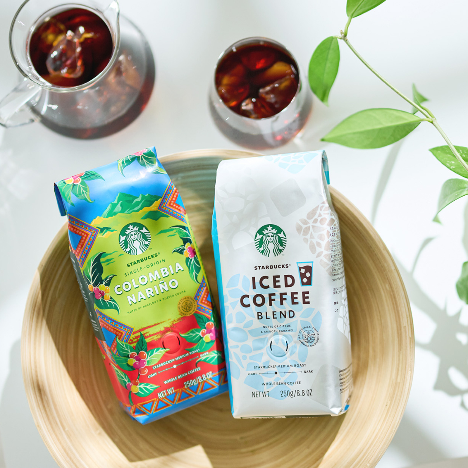白いテーブルの上に置かれたスターバックス® シングルオリジン コロンビア ナリニョとスターバックス® アイスコーヒー ブレンドのパッケージ、グラスに注がれたアイスコーヒー
